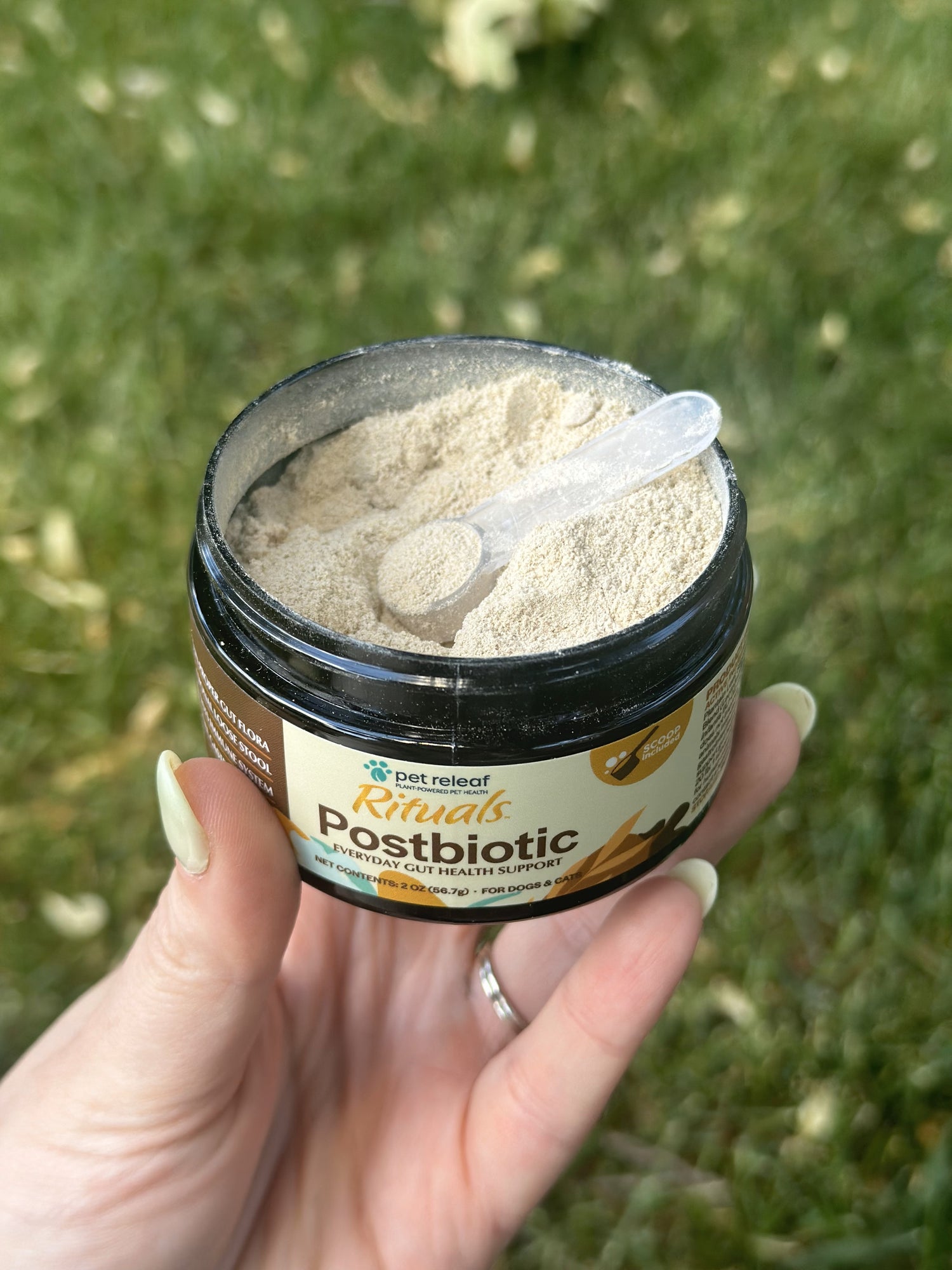 Hand holding a container of Rituals Postbiotic powder with scoop.